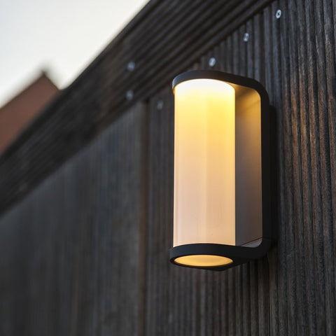 A cylindrical outdoor wall light mounted onto a fence.