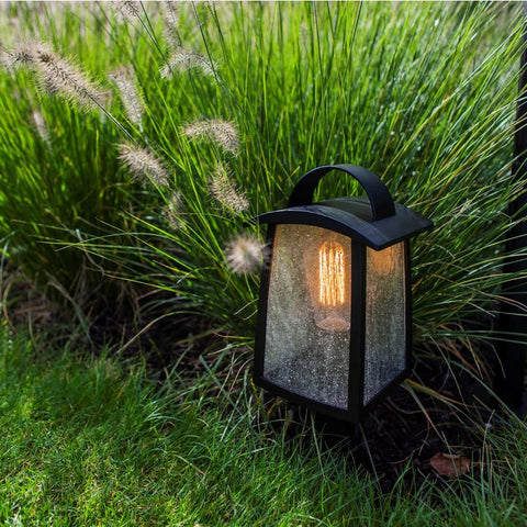 A lantern style outdoor light amongst some grass.
