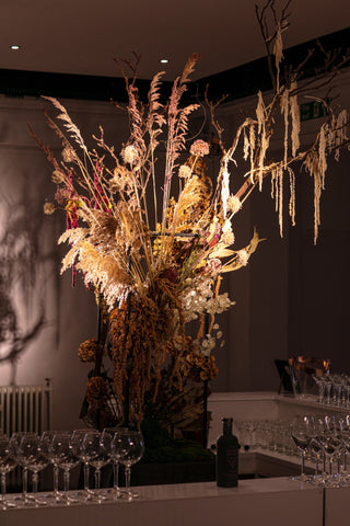 Sculptural dried flower arrangement displayed in the centre of a drinks bar. Its is dramatically lite with strong lighting