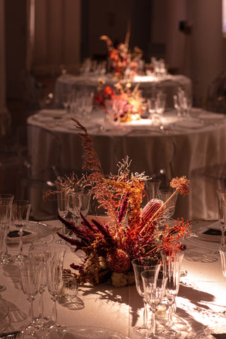 dried flower arrangement on a round dinning table. The dried flowers are red, beige and gold