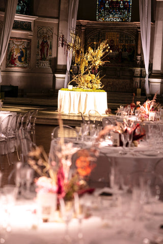 A large dried flower display in the middle of a church. It has wild branches and is dramatically lit with stage lighting.