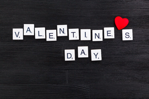 Against a black wood background, Valentine's Day is spelled out with Scrabble Letters