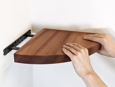 A mahogany corner floating shelf being slid onto a bracket