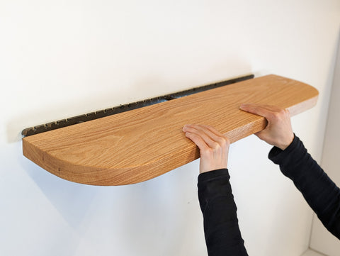 Hands push an oak mahogany floating shelf into its secure bracket