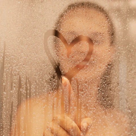 woman drawing heart on shower glass