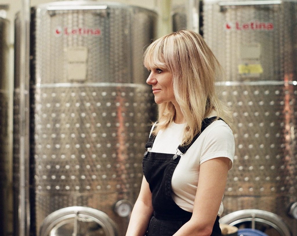 blond woman standing in front of metal brewery equipment