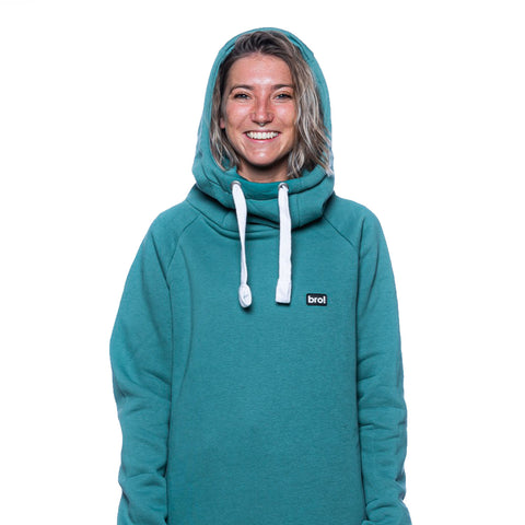 This image shows a woman wearing the bro! chill n'shred hoodie (spruce green colourway) with the hood up. The image is to illustrated the built in neckwarmer functionality of the hood.