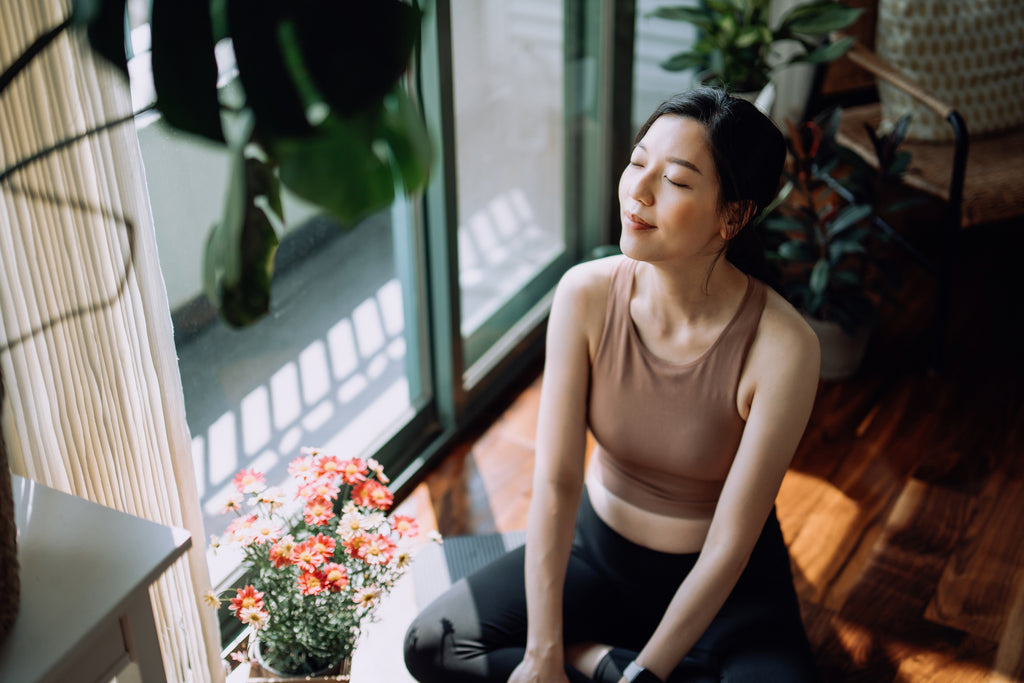 Woman taking a break after working out at home, sitting on an exercise mat, and taking a deep breath with her eyes closed