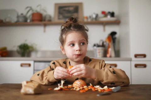 Young girl eating an orange at the kitchen table