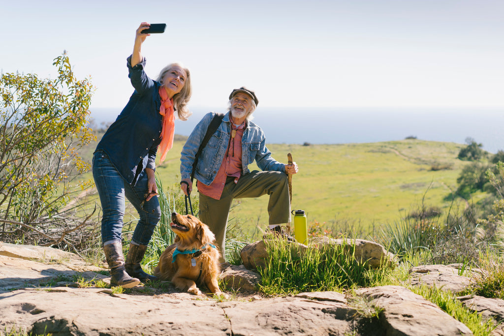 Senior couple taking a selfie with dog during a hike on a sunny day.