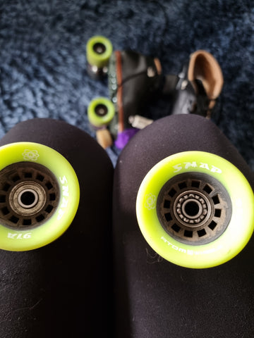 Yellow roller skate wheels. The left wheel's bearings are intact. The right wheel has no bearing shield, so the ball bearings are visible.
