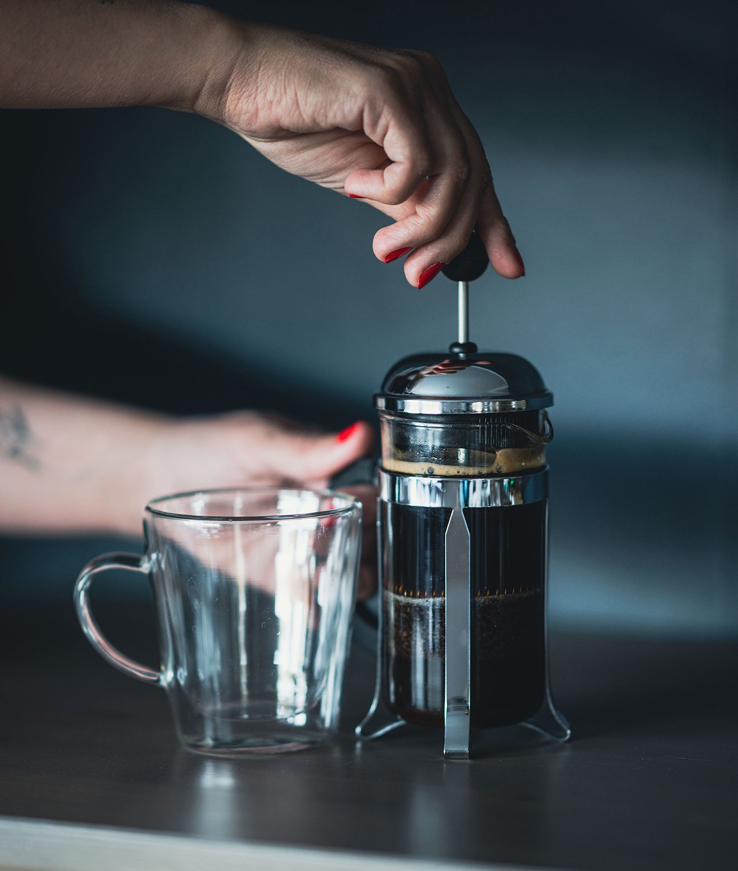 Woman pressing French press next to glass mug