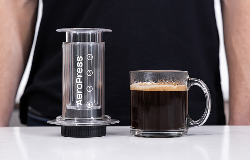 AeroPress Clear and Flow Control Filter Cap next to mug of rich coffee