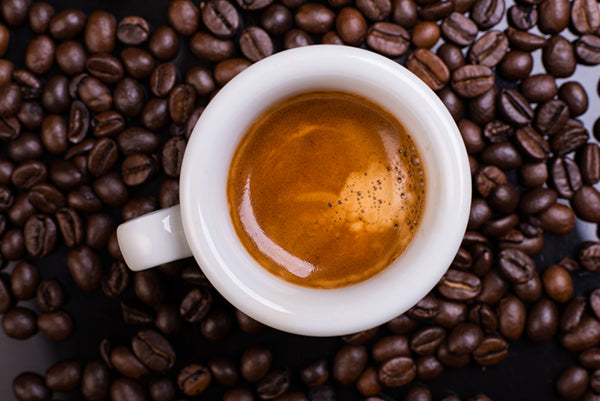 A small cup of espresso with crema on top of coffee beans