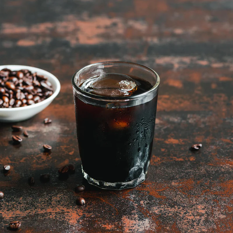 Glass of iced coffee next to dish of coffee beans