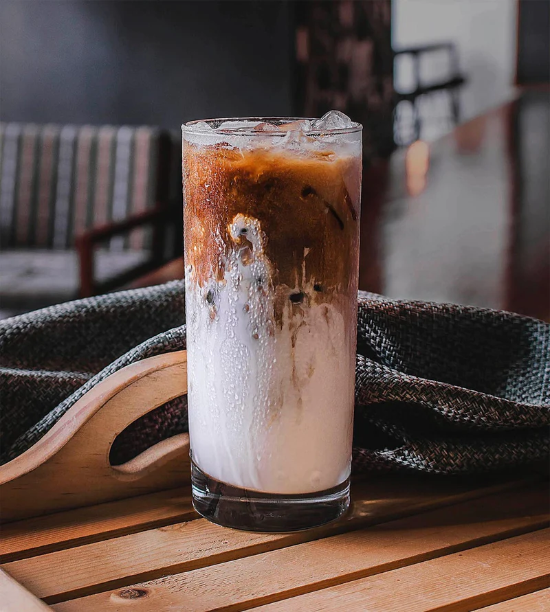 Cold brew coffee over ice with cream on wooden tray