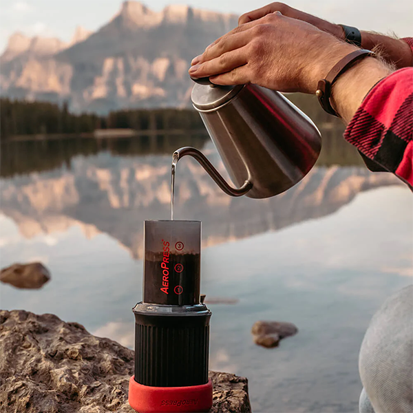 Pouring water into AeroPress Go next to mountain lake