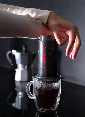 https://cdn.shopify.com/s/files/1/0601/8783/6659/files/Person-brewing-coffee-with-AeroPress-Original-coffee-maker-in-front-of-moka-pot_480x480.jpg?v=1673480799