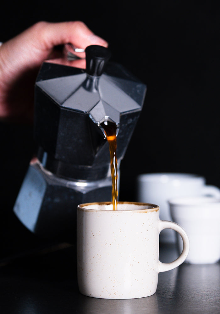 Pouring coffee out of moka pot into white mug