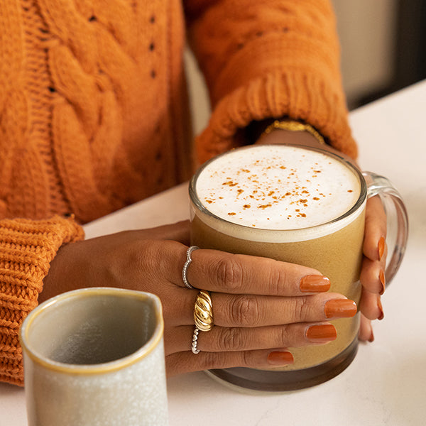 Woman with orange sweater holding pumpkin spice latte