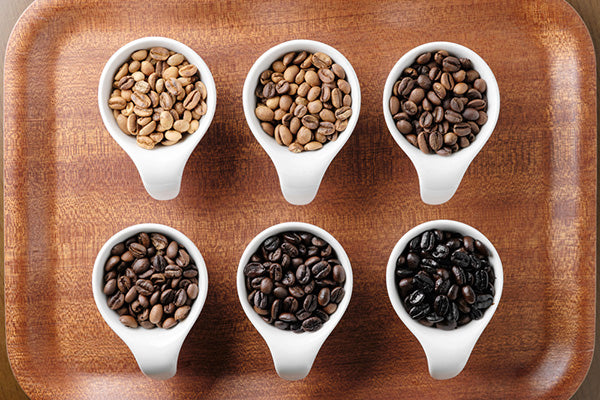 Six white cups with different roast coffee beans inside on a wood tray