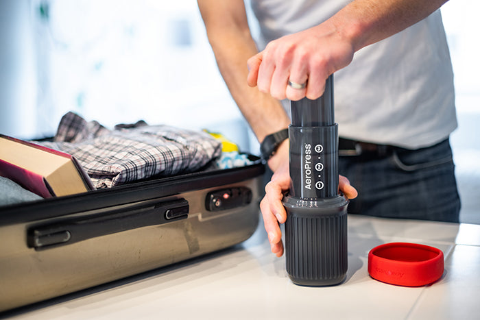 Using AeroPress Go travel coffee maker next to suitcase