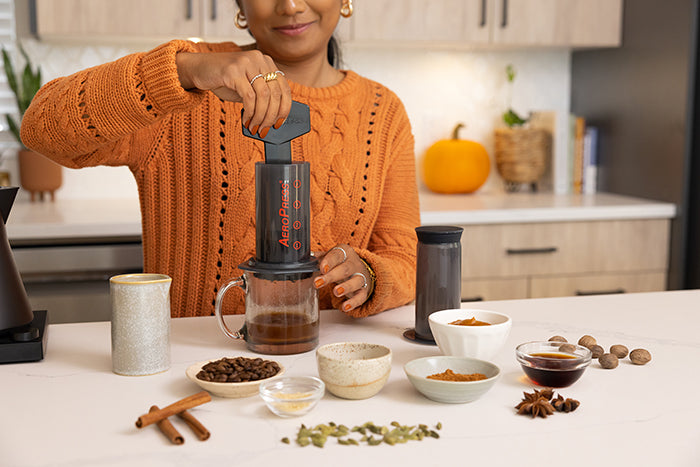 Woman stirring coffee and hot water in AeroPress coffee maker while making a pumpkin spice latte