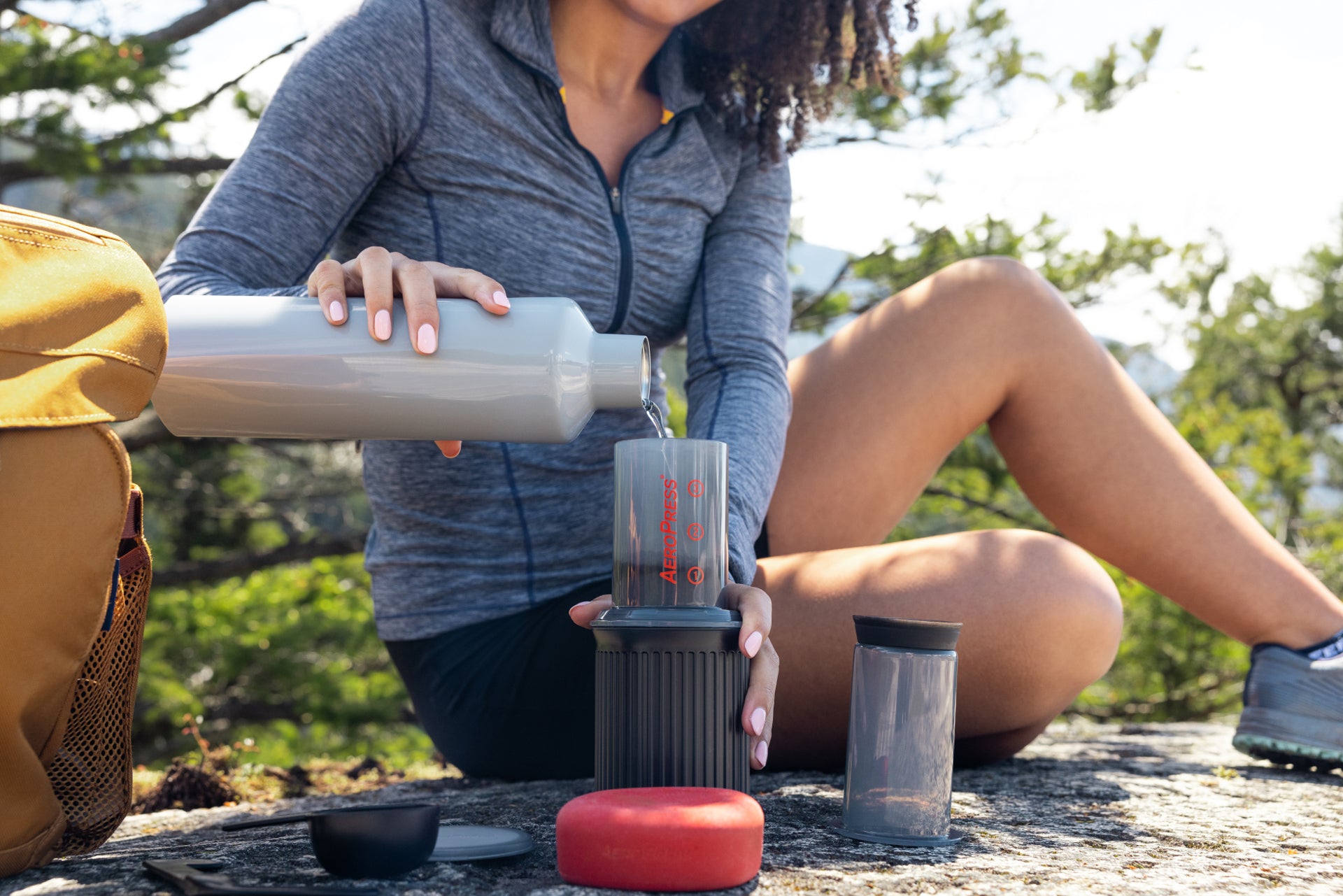 Woman pours hot water into AeroPress Go while backpacking
