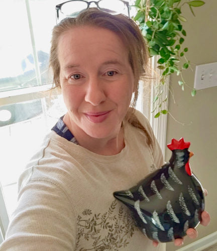 Shannon, a blonde haired woman holds a ceramic black chicken while smiling.