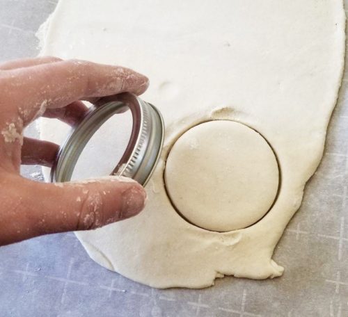 A hand is holding a jar lid after just imprinting the rolled out salt dough with it.