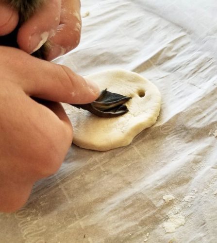 A hand gently holds and pressed a ducklings foot into a salt dough ornament to make an imprint.