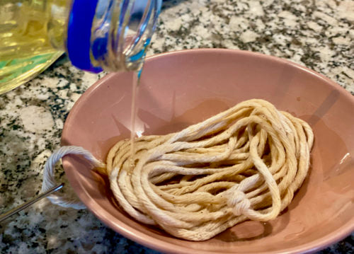 A section of twine lays in a pink bowl as olive oil is being poured on it.