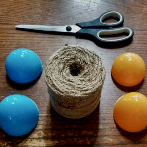 Supplies needed to make a jute bunny egg including a roll of jute, a pair of scissors, and two plastic eggs. 