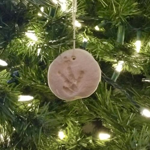 Salt dough chicken print ornament hanging from a Christmas tree with white lights.