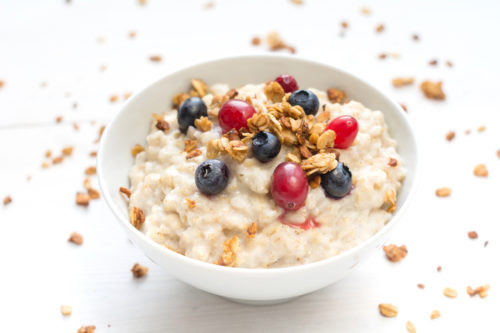 A cold-weather treat of a bowl of porridge with fresh fruit and granola sit on a white table. 