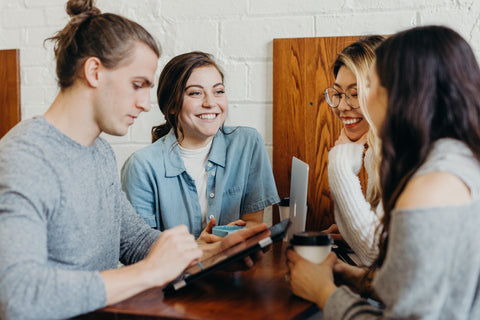 four young people sitting around a table and enthusiastically overlooking a tablet and engaged in a conversation