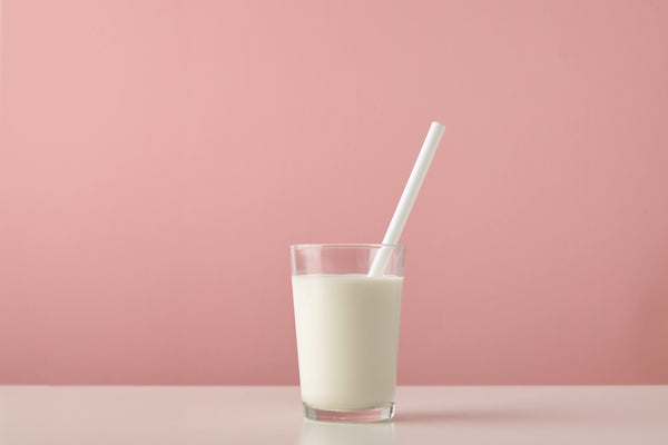 A glass of calcium fortified oat milk resting on a table with a pink background