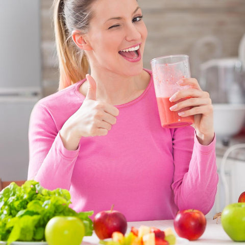Happy woman blinking and giving thumbs up with a cup of fruit juice and healthy foods on the table