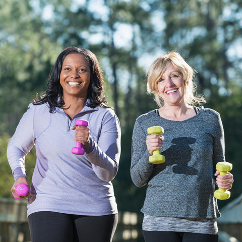 Two older women with dumbbells on their hands power walking outdoors