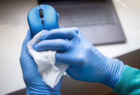 A person in blue gloves sanitizes a mouse with an antimicrobial spray, protecting against germs