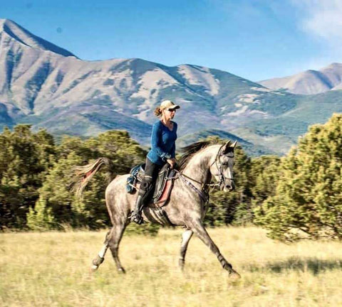 Female endurance competitor Tammy Gagnon riding her horse in Freeform Classic Cutback Treeless Saddle with mountains in the background.