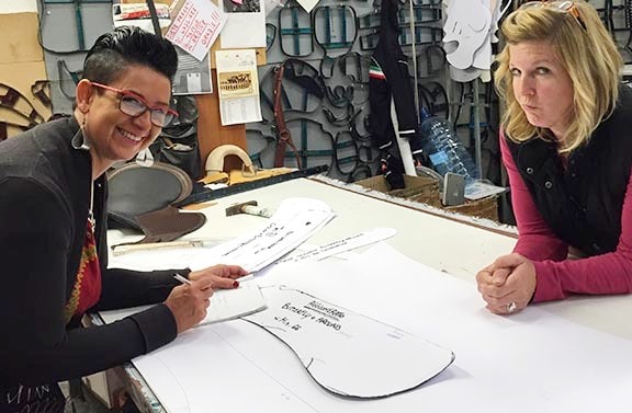 Two Italian craftswomen leaning over a table looking at Freeform Treeless saddle production pieces in Italy.