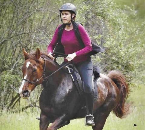 Endurance rider wearing a helmet cantering her chestnut Arabian mare in a Freeform treeless saddle on an endurance ride.