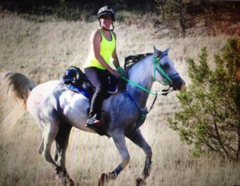 Woman cantering her gray Arabian horse on an endurance ride using a Freeform treeless saddle.