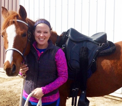 Young woman standing next to her sorrel color horse wearing a Freeform treeless saddle.