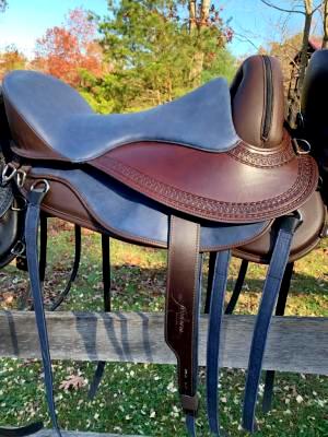 Brown Freeform Pathfinder treeless saddle with leathers sitting on a fence with fall foliage in the background.