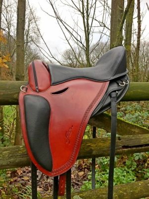 Rust and black treeless saddle on a fence with woods in the background - Freeform Pathfinder PJ.