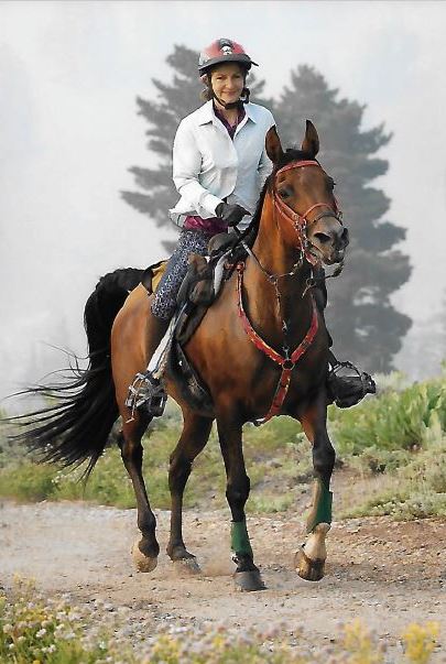 Endurance rider Suzanne Huff riding her bay horse on a trail with trees in the background in a Freeform classic treeless saddle with the ultimate trail seat.