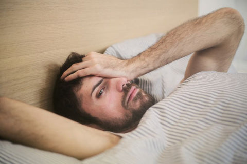man in bed rubbing his eyes