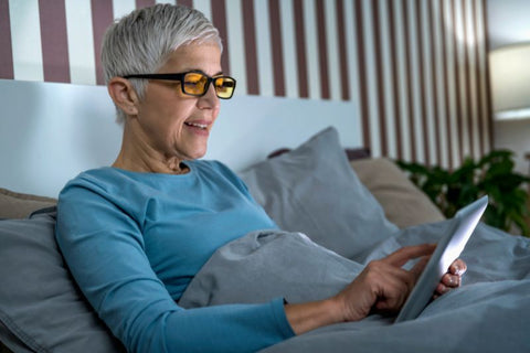 older woman wearing blue light blocking glasses in bed